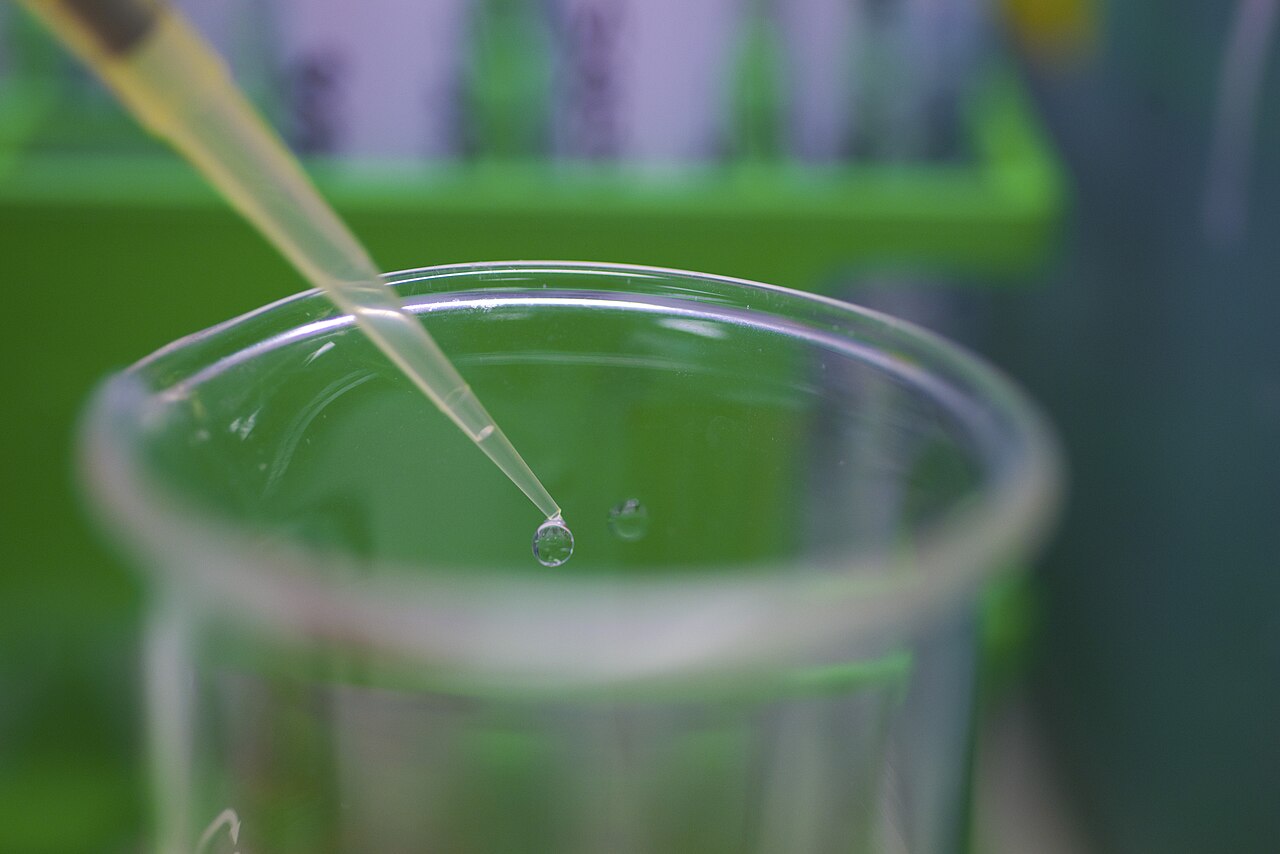 Close-up of a reagent droplet at the tip of a pipette in an analytical chemistry laboratory.